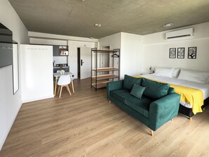 Ein modernes Hotelzimmer mit Bett, grünem Sofa, Schreibtisch mit Stuhl und Kleiderschrank.