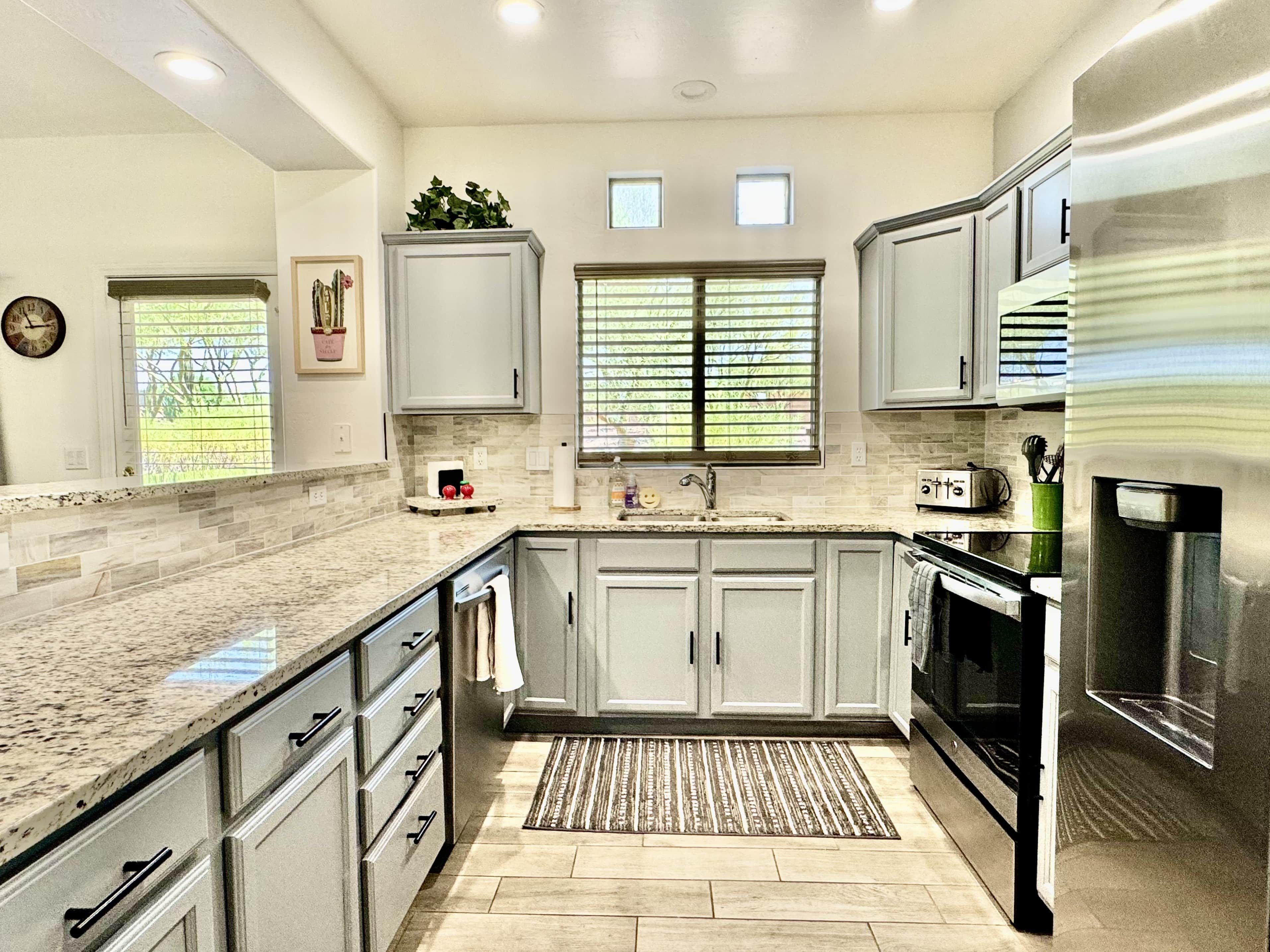 A modern kitchen with granite countertops, stainless steel appliances, and a large window with blinds.