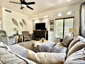 A living room with a sofa, armchair, and a television on a wooden cabinet. - Vistoso Resort Condo #107A (Oro Valley)