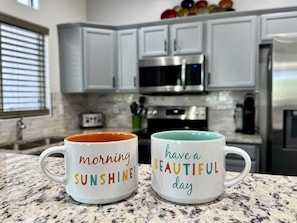 Two mugs on a kitchen counter with a modern design, a microwave, and cabinets in the background. - Vistoso Resort Condo #107A (Oro Valley)
