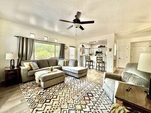A spacious living room with a sofa, ottoman, and a patterned rug. - Vistoso Resort Condo #107A (Oro Valley)