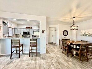 A modern kitchen with white cabinets, a bar area, and a dining space with a wooden table and chairs. - Vistoso Resort Condo #107A (Oro Valley)