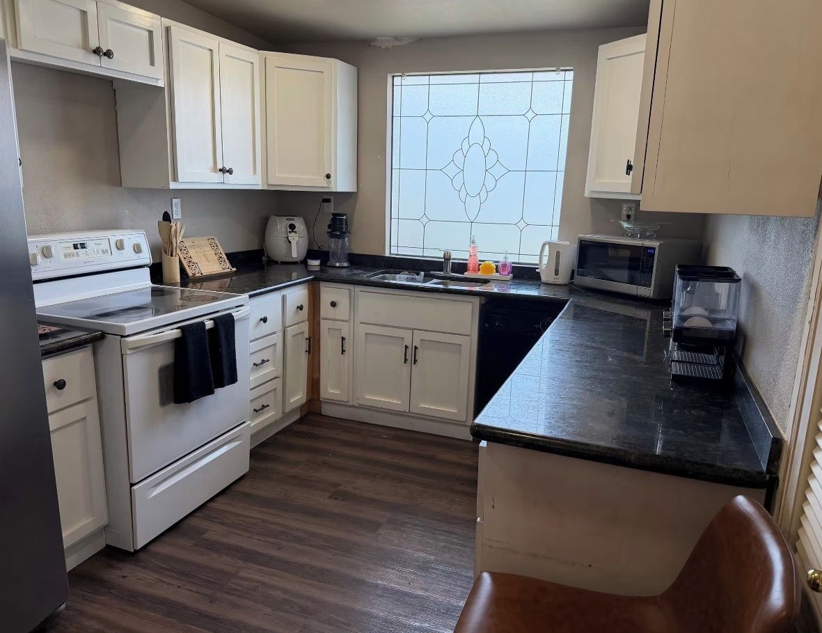 A kitchen with white cabinets, a stove, a microwave, and a window with a decorative pattern.