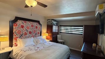 A bedroom with a bed, a ceiling fan, a window with blinds, a nightstand, and a lamp.