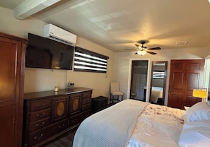 Ein Schlafzimmer mit Bett, Kommode, Fernseher, Deckenventilator und einer Tür zu einem anderen Raum.