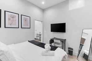 A modern hotel room with a bed, a desk, a chair, a TV, and artwork on the wall. - 3 APTS Side-by-Side 3BR/3BA- 20 min to Manhattan 2 (Newark)