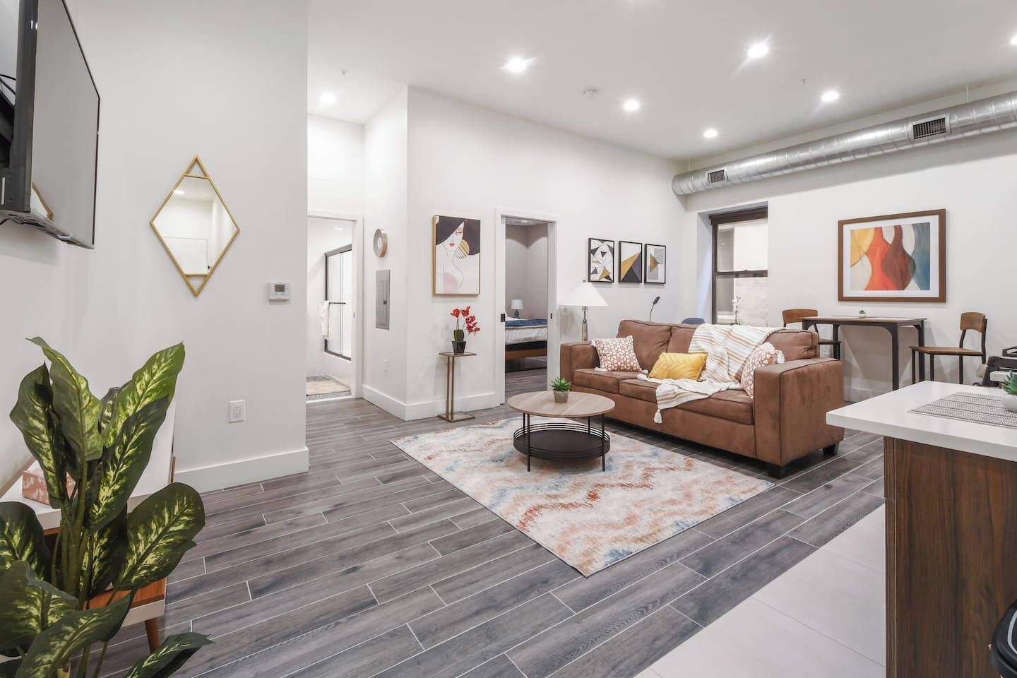 A modern living room with a brown sofa, a coffee table, and a rug. There is a dining area with a table and chairs.