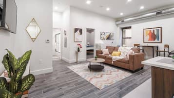 A modern living room with a brown sofa, a coffee table, and a rug. There is a dining area with a table and chairs.
