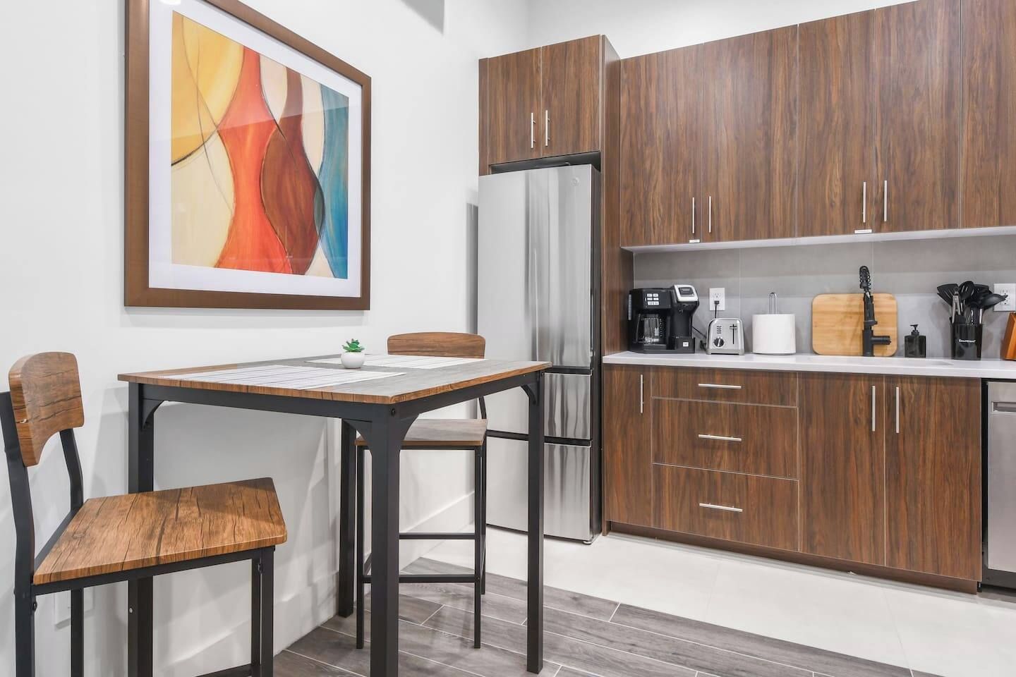 A modern kitchen with wooden cabinets, a stainless steel refrigerator, a coffee maker, and a toaster.