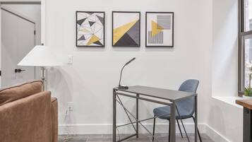 A modern room with a desk, chair, and a lamp. There are three framed abstract artworks on the wall.