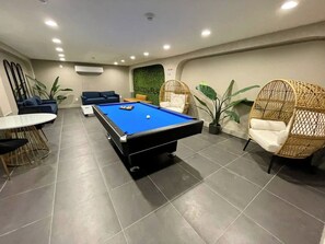 A pool table in a room with a tiled floor, a sofa, and two wicker chairs. - 1BR 20 Min Manhattan 2 min prud center. Concerts! (Newark)