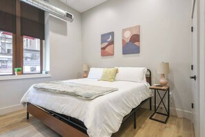 Quarto com cama, luminárias de cabeceira, janela com vista e arte abstrata nas paredes.