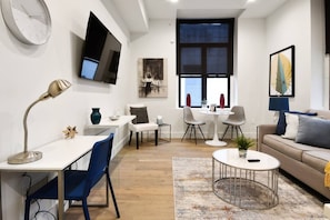 A modern living room with a sofa, coffee table, and a dining area with chairs and a table. - Charming 1BR King Bed - Just 20 Minutes from NYC! (Newark)