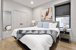 A modern bedroom with a large bed, bedside lamps, a window, and a painting on the wall. - Charming 1BR King Bed - Just 20 Minutes from NYC! (Newark)