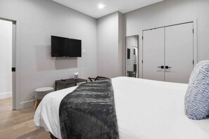 Quarto de hotel moderno com cama, escrivaninha, cadeira, televisão e guarda-roupa.