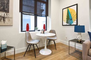 A modern room with a round table, two chairs, a lamp, and a painting on the wall. - Charming 1BR King Bed - Just 20 Minutes from NYC! (Newark)