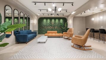Ein modernes Wohnzimmer mit grüner Wand, blauen und orangefarbenen Sofas, einem weißen Couchtisch und einer Sitzecke mit einer Bar.
