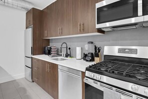 A modern kitchen with stainless steel appliances, wooden cabinets, and a white countertop. - 1BR King 20 min from NYC! 2 minutes to prudential (Newark)