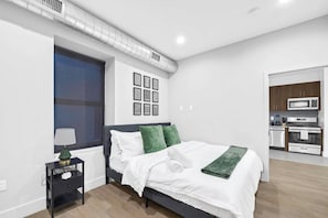 Un dormitorio moderno con cama, mesita de noche y vistas a una cocina.