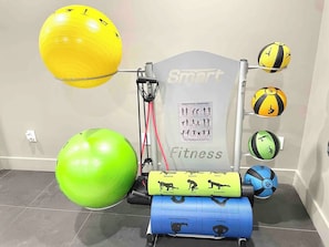 Un gimnasio con equipo de ejercicio, incluyendo un entrenador de resistencia, pelotas de ejercicio e ilustraciones relacionadas con el estado físico.