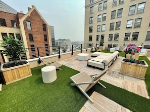 Una terraza en la azotea con mobiliario exterior, macetas y vistas a la ciudad.