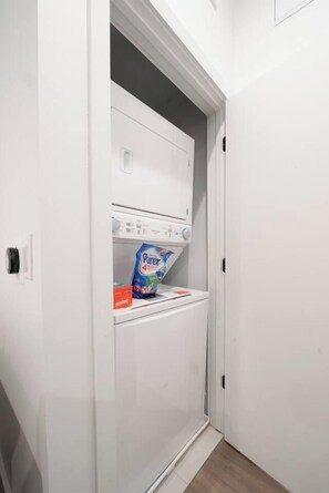Un lavadero pequeño y blanco con lavadora y secadora integradas, un estante con detergente y un espacio de almacenamiento.