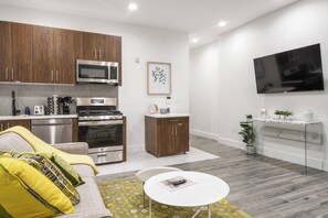 Eine moderne Küche mit Edelstahlgeräten, eine Essecke mit einer Couch und einem Couchtisch sowie ein Flachbildfernseher an der Wand.
