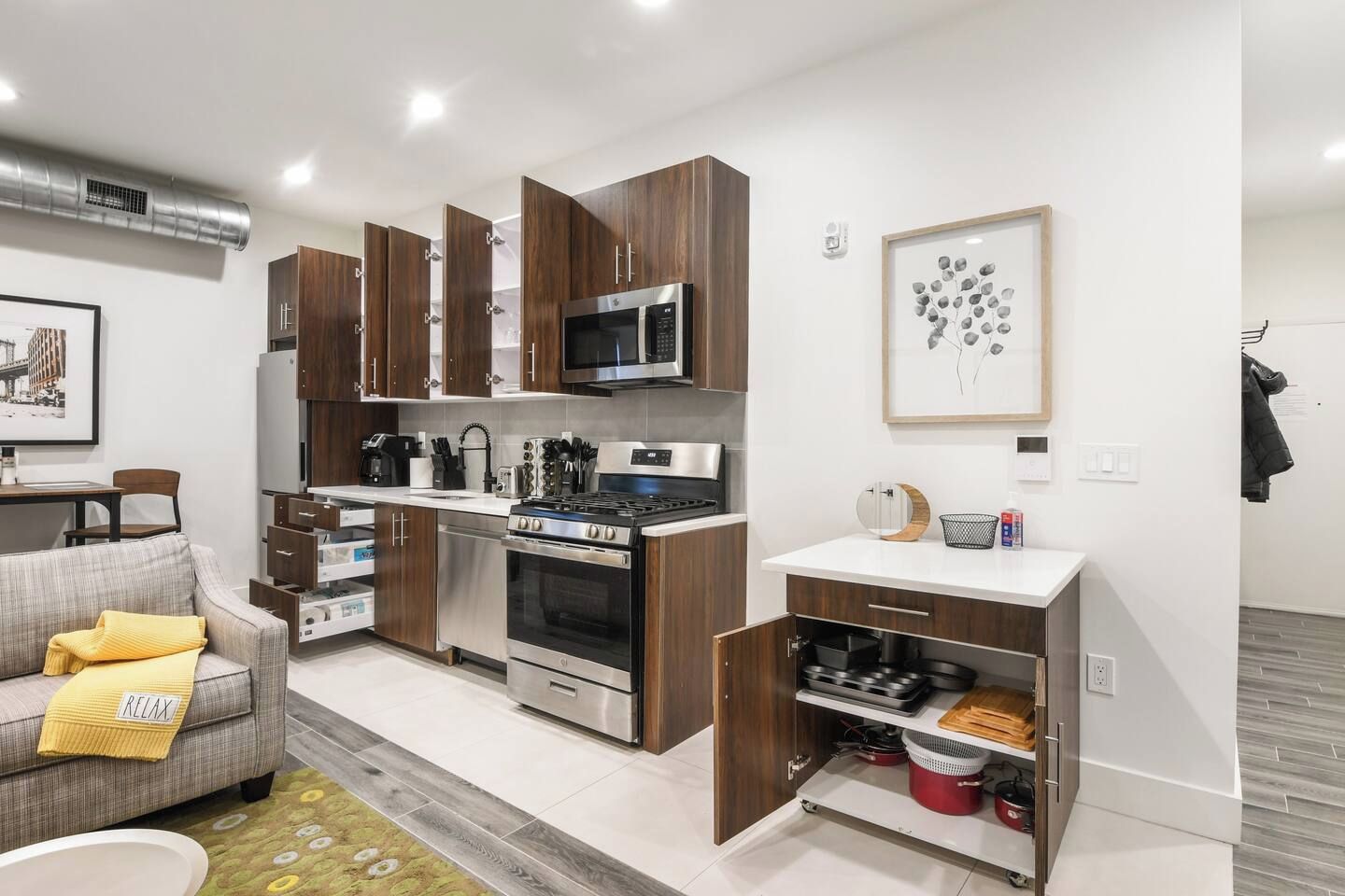 A modern kitchen with wooden cabinets, stainless steel appliances, and a dining area with a grey sofa.