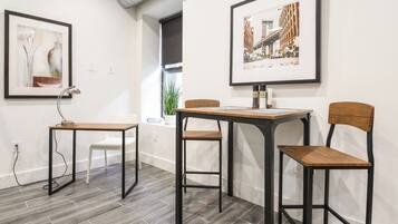 A modern room with a wooden table and chairs, a desk with a lamp, and two framed pictures on the wall.