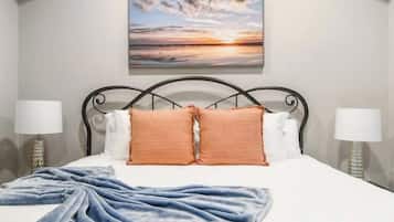A hotel room with a bed, two bedside lamps, a painting on the wall, and a ceiling vent.