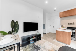 A modern living room with a flat-screen TV, a dining area with a table and chairs, and a kitchen with wooden cabinets and a built-in oven. - Monthly friendly Lux 1BR 20 Min NYC 4 min to Prud (Newark)