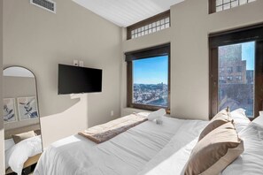 Een hotelkamer met een bed, een flatscreen televisie, een raam met uitzicht op de stad en een spiegel.