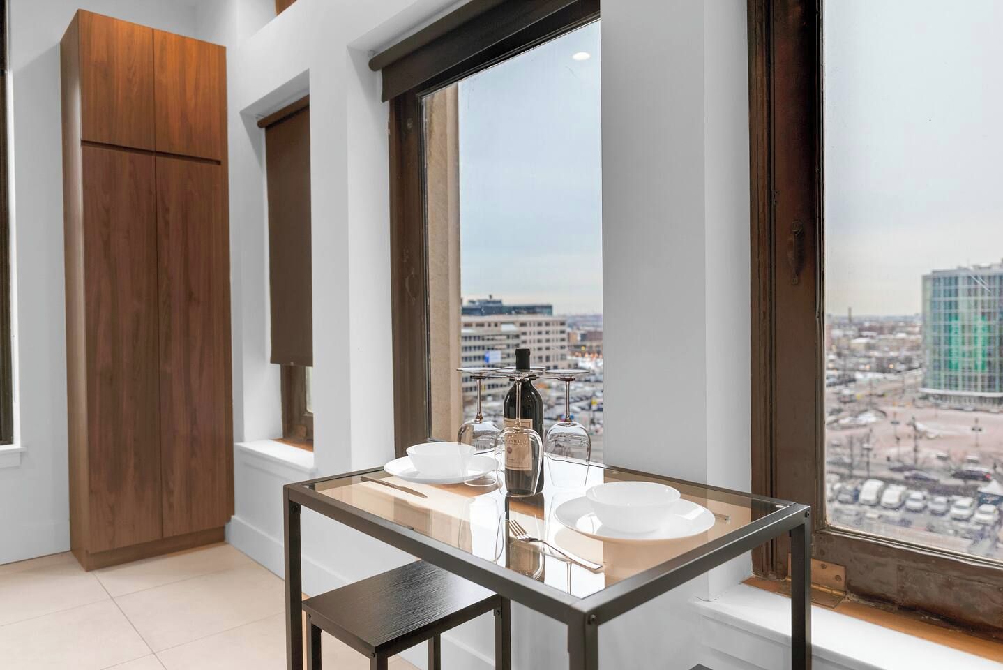 A modern room with a dining table, a wine bottle, and a view of a cityscape through large windows.
