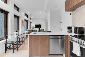 Een moderne keuken met een centraal eiland, roestvrijstalen apparatuur en een eethoek met een glazen tafel.