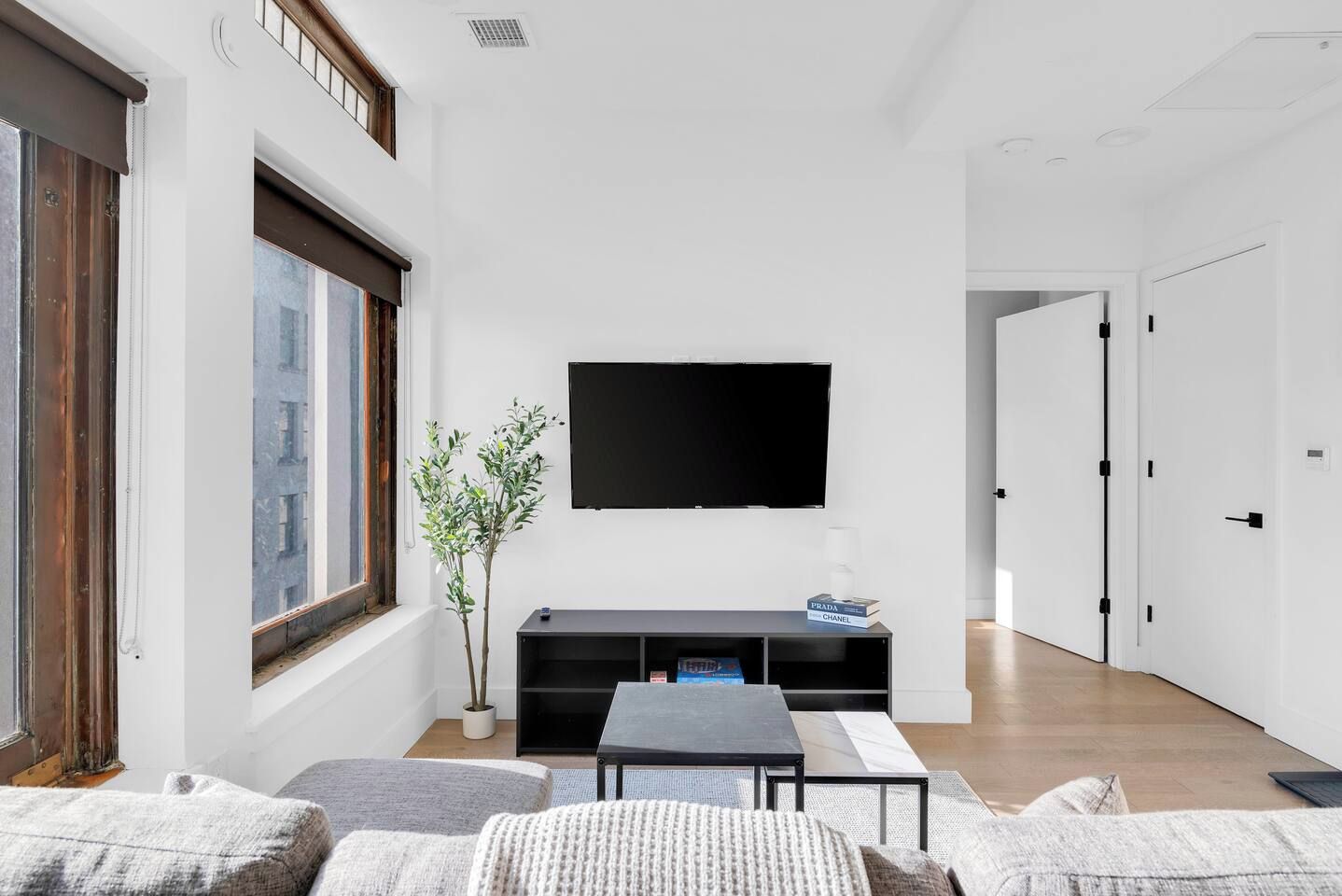 A modern living room with a flat-screen TV mounted on the wall, a black entertainment unit, a potted plant, and a sofa.