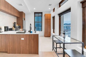 A modern kitchen with wooden cabinets, a central island, and a view of the city through large windows. - 20 Min to NYC Modern Lux Escape– 1BR, Gym rooftop (Newark)