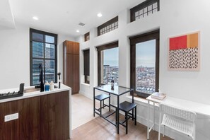 A modern kitchen with a wooden counter, a dining area with a glass table, and large windows offering city views. - 20 Min to NYC Modern Lux Escape– 1BR, Gym rooftop (Newark)