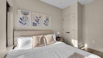 A bedroom with a large bed, a nightstand, a wardrobe, and three wall-mounted artworks.