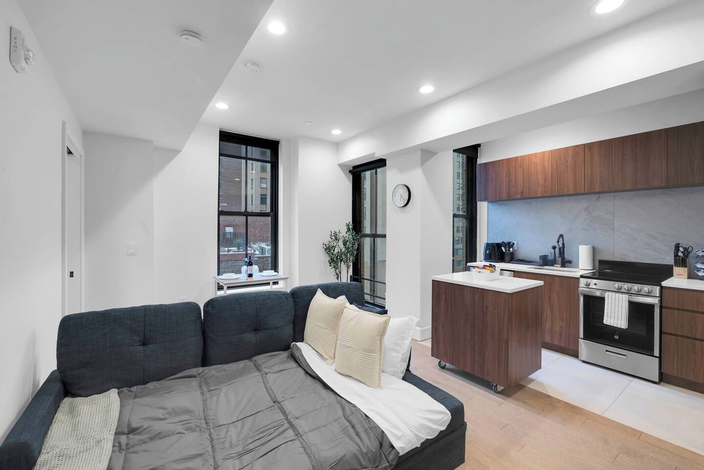 A modern apartment with a sofa, a small kitchen with a stove, and a window with a view of the city.