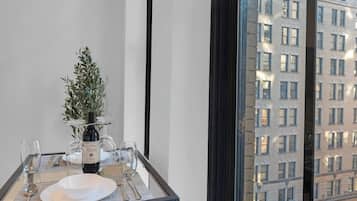 A dining table set with a bottle of wine, glasses, and a small plant, with a view of a building through a window.