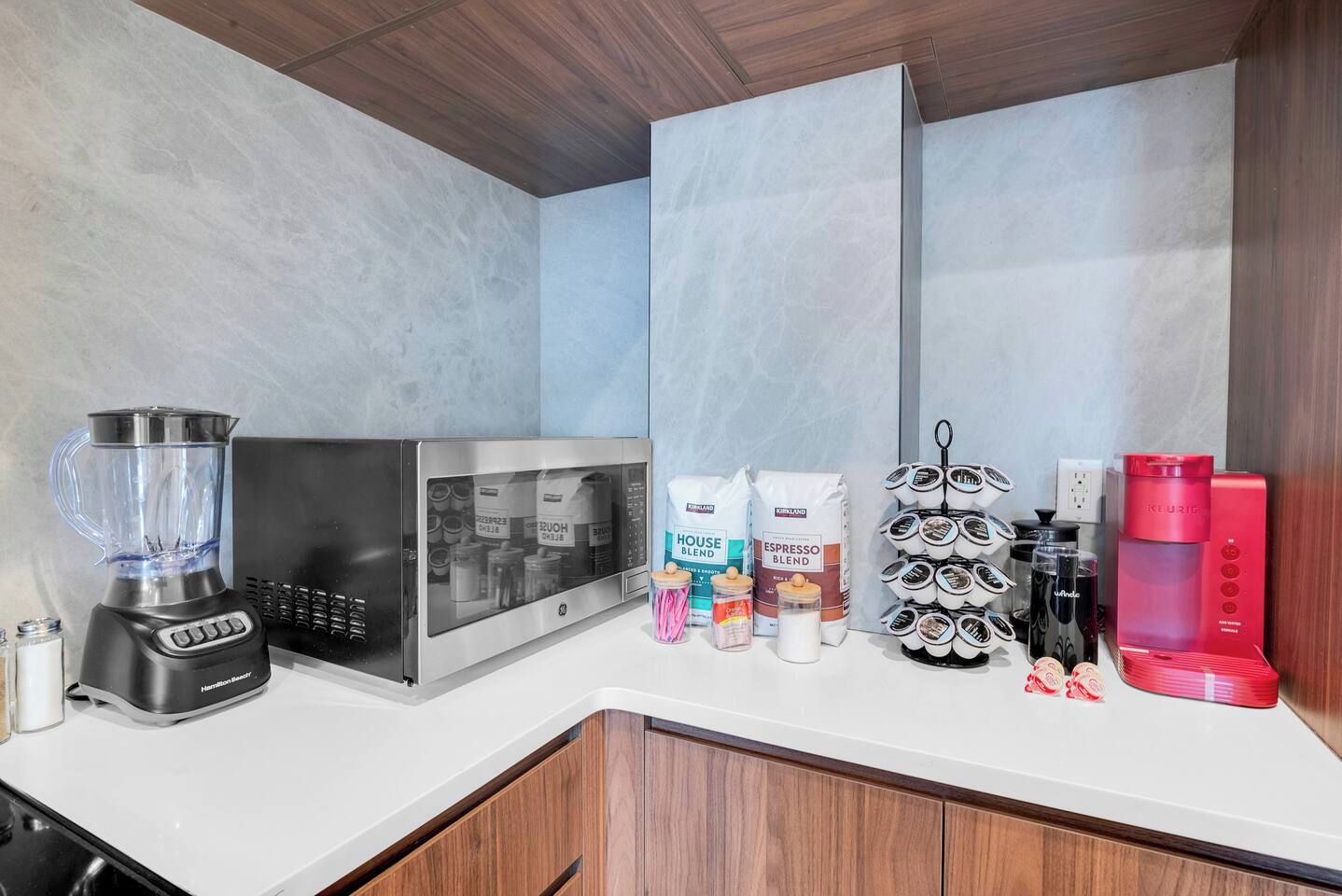 A kitchen with a blender, microwave, coffee maker, and coffee pods.