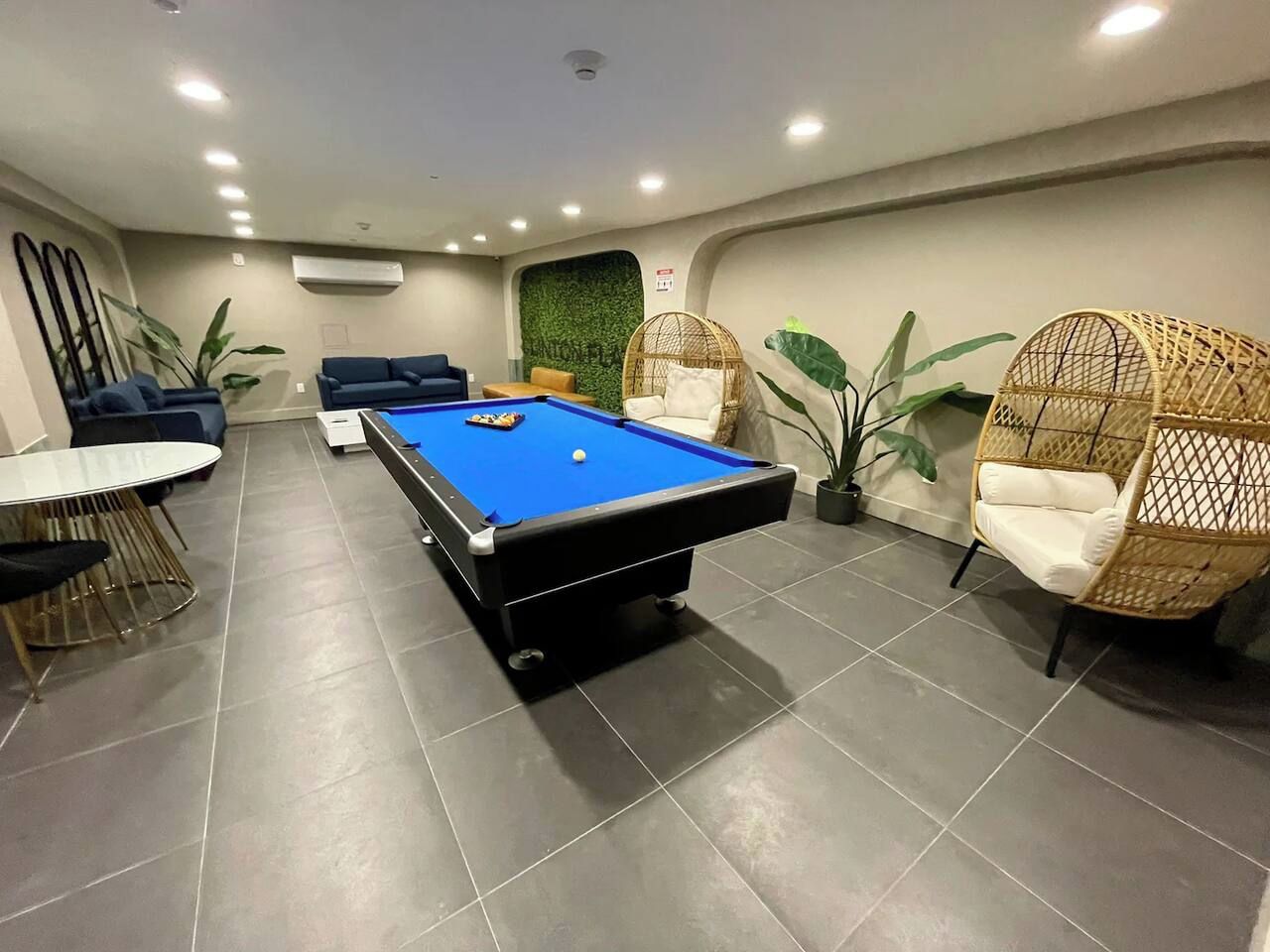 A pool table in a room with a tiled floor, a sofa, and two wicker chairs.