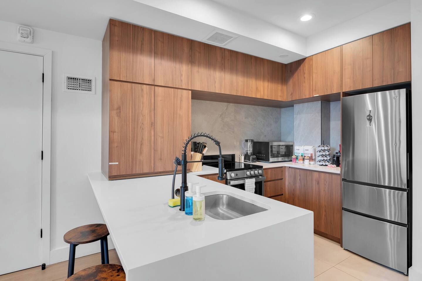 A modern kitchen with wooden cabinets, a stainless steel refrigerator, a built-in oven, and a sink with a faucet.