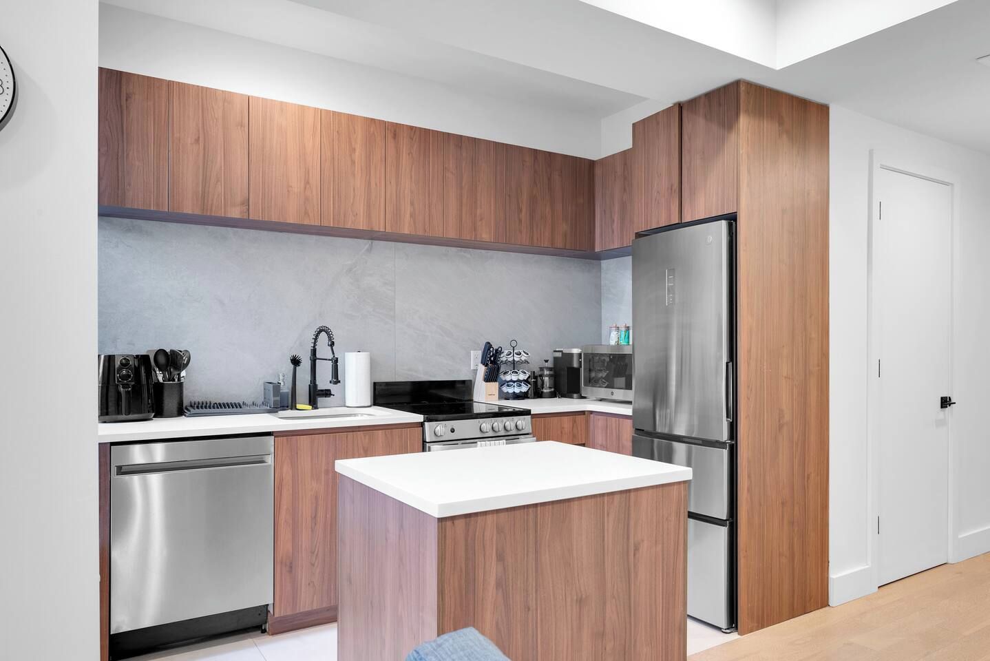 A modern kitchen with wooden cabinets, stainless steel appliances, and a white countertop.