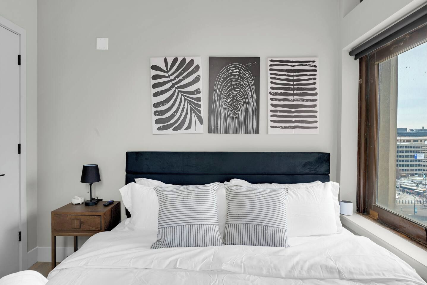 A bedroom with a bed, a nightstand, a lamp, and three wall art pieces.
