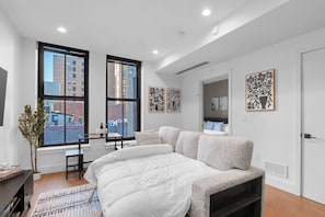 Une chambre moderne avec un grand lit, un bureau et une vue sur la ville grâce à de grandes fenêtres.