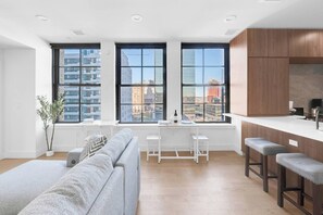 A modern apartment with a kitchen, dining area, and a large window with a city view. - Lux King 1BR 20 Min NYC 4 MIN to Prudential/Penn (Newark)