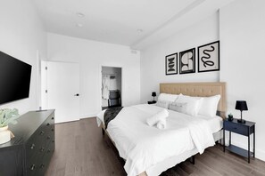 A modern bedroom with a large bed, a television, a wardrobe, and a bathroom visible through an open door. - Central Stylish 1BR Free Parking Lux Fabulous King (Plainfield)