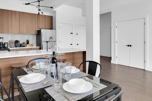 A modern kitchen with a central island, white cabinetry, and a dining area set with a table, chairs, and glassware. - Central Stylish 1BR Free Parking Lux Fabulous King (Plainfield)
