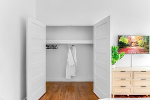 Een inloopkast met houten vloer, een witte deur en een aan de muur bevestigde televisie die een tuin toont.